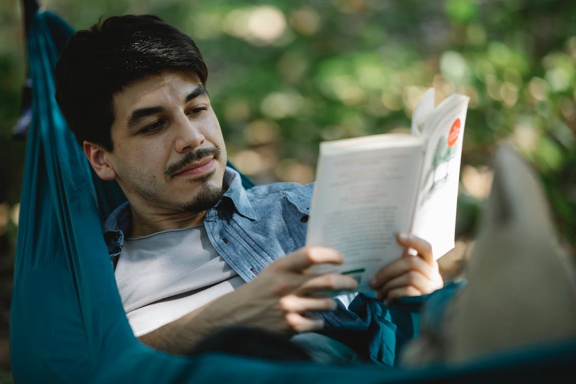 man reading a book outdoors in a hammock